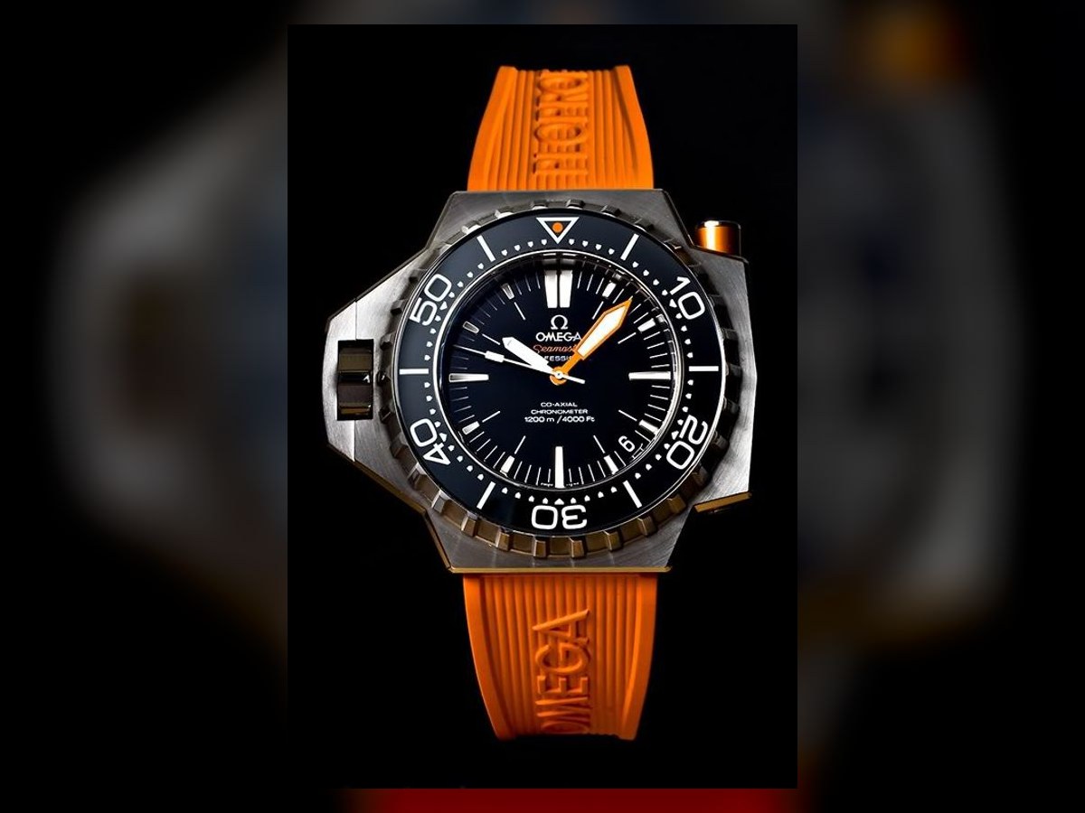 The Omega Seamaster Ploprof dive watch, steel case and orange rubber strap, lit dramatically on a black background.
