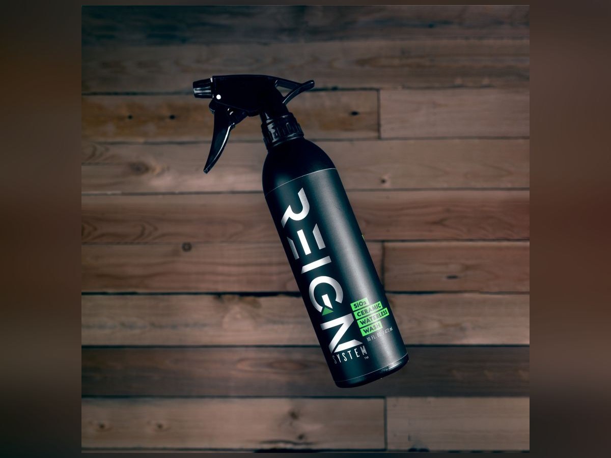 Matte black Reign System SiO2 Ceramic Waterless Wash spray bottle on a dark wood background.